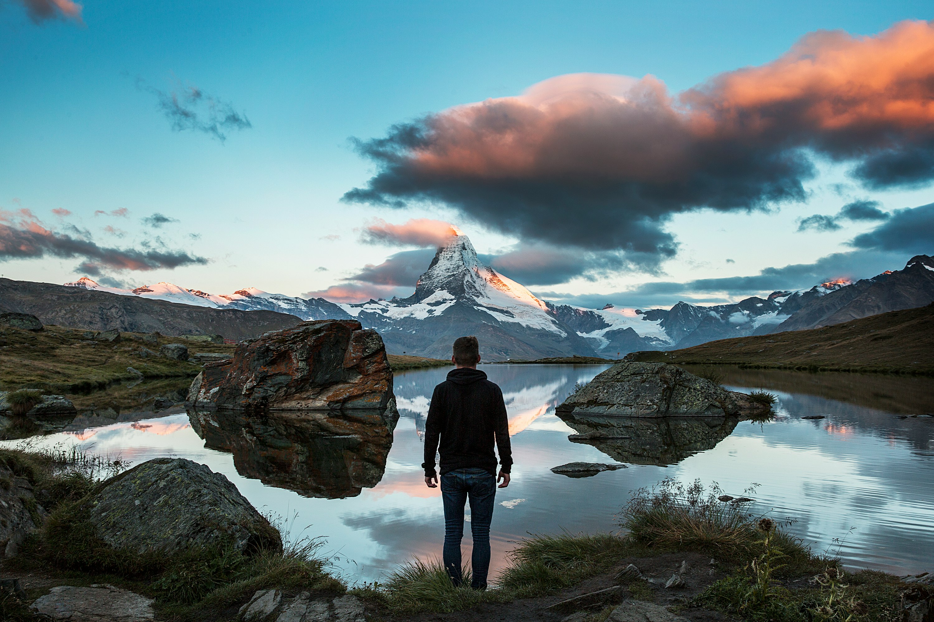 man standing on rocky cliff facing body of water